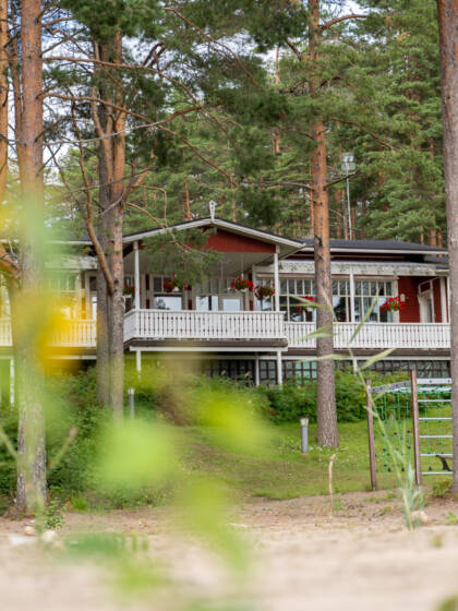 Sääksin leirikeskuksen rakennus, etualalla hiekkaa ja puita.