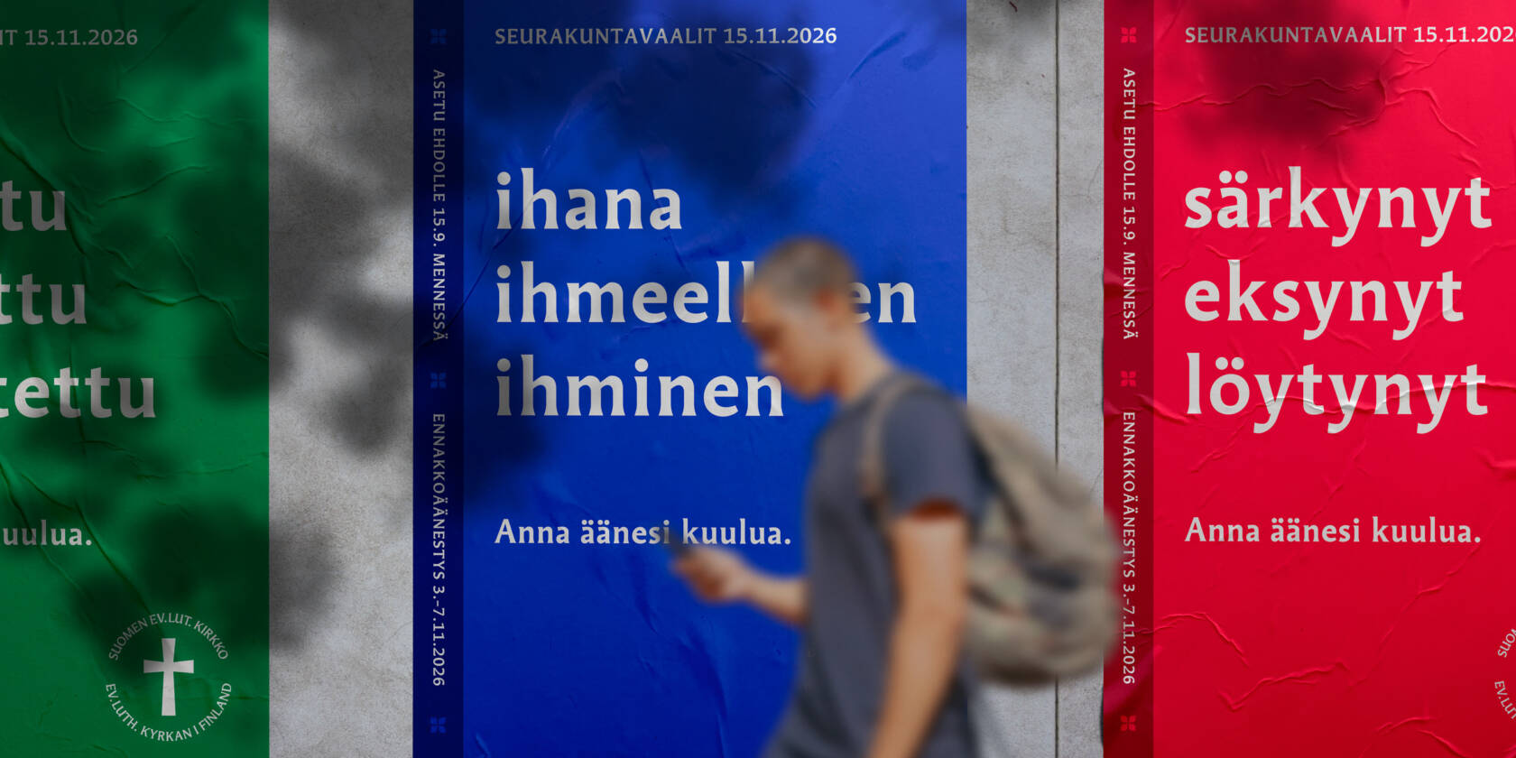 Seurakuntavaalien julisteita seinällä, julisteen tekstinä ihana ihmeellinen ihminen, ihminen puhelin kädessä kävelee ohi,