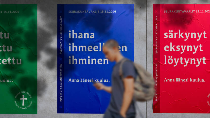 Seurakuntavaalien julisteita seinällä, julisteen tekstinä ihana ihmeellinen ihminen, ihminen puhelin kädessä kävelee ohi,
