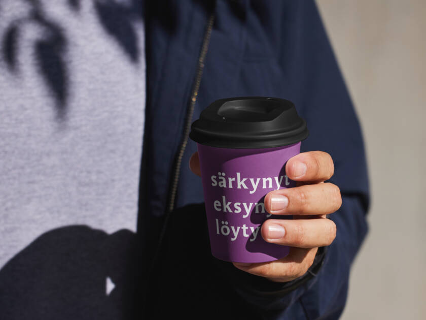 Ihminen kertakäyttökahvimuki kädessä, mukissa painatus särkynyt, eksynyt, löytynyt.