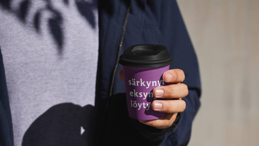 Ihminen kertakäyttökahvimuki kädessä, mukissa painatus särkynyt, eksynyt, löytynyt.