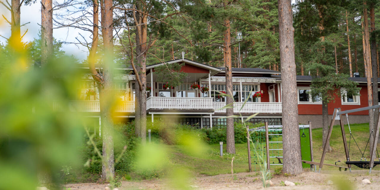 Sääksin leirikeskuksen rakennus, etualalla hiekkaa ja puita.