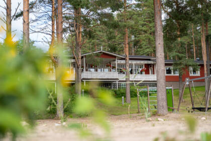 Sääksin leirikeskuksen rakennus, etualalla hiekkaa ja puita.
