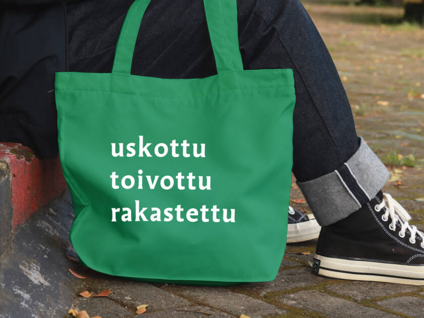Ihmisen jaloissa kangaskassi, jossa lukee uskottu, toivottu, rakastettu.