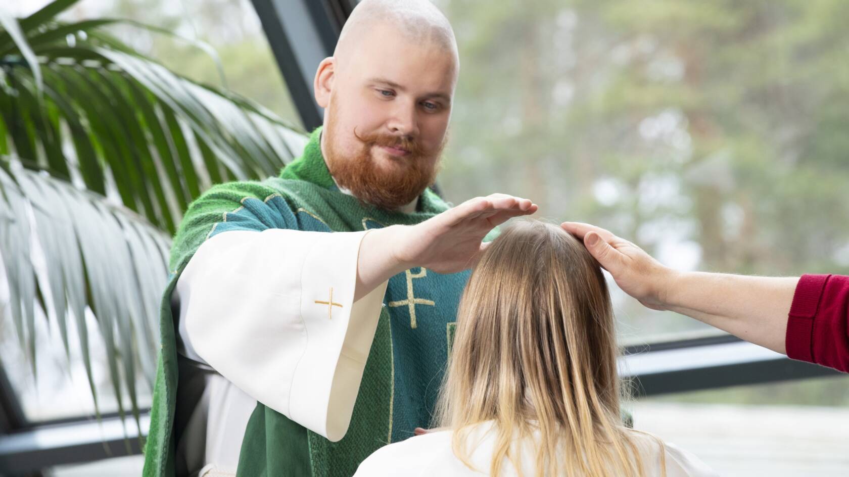 Pappi ja kummi siunaavat alttarille polvistunutta rippikoululaista.