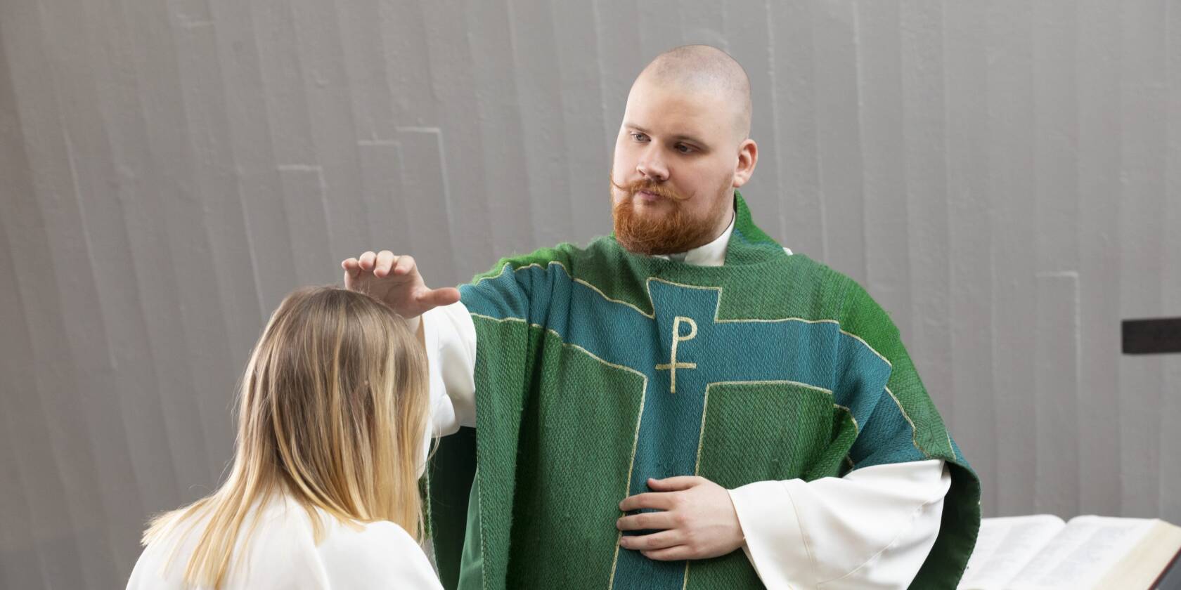 Pappi siunaa alttarille polvistunutta rippikoululaista.