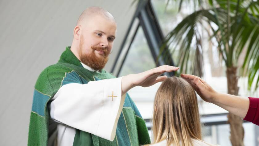 Pappi ja kummi siunaavat konfirmaatiossa.