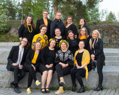 Kuorolaisia istuu ja seisoo ryhmässä kolmessa rivissaä