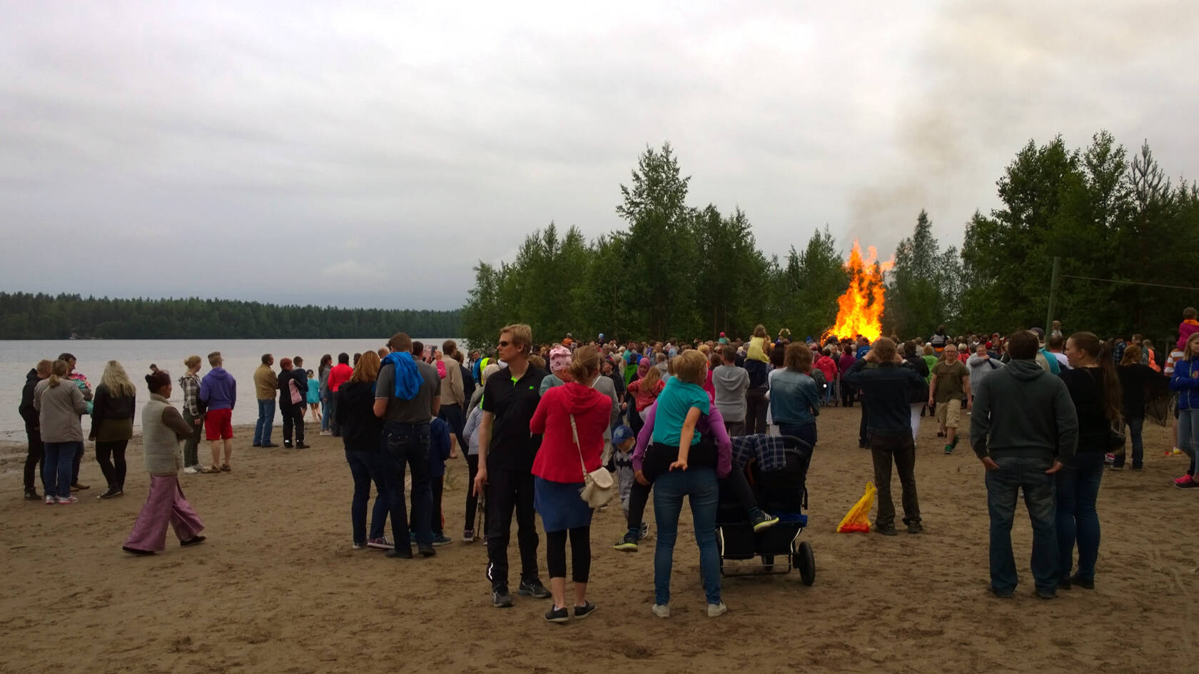 Paljon ihmisiä juhannuksena Sääksin rannalla, taustalla kokko.