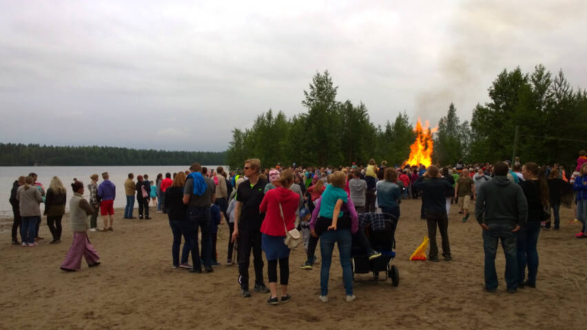 Paljon ihmisiä juhannuksena Sääksin rannalla, taustalla kokko.