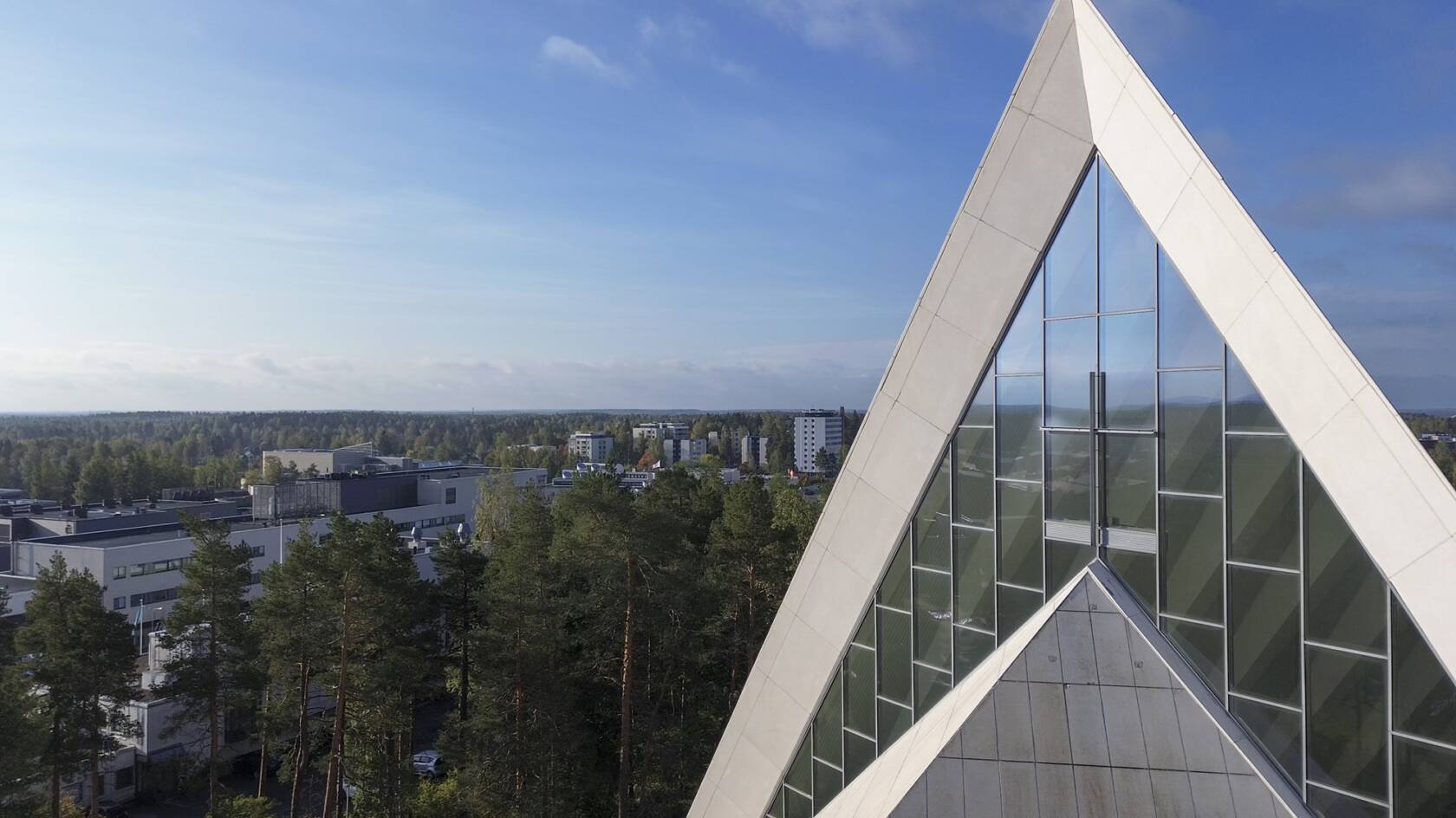 ilmakuva hyvinkään kirkon etupuolelta, sinistä taivasta vasten näkyy kirkon päätyikkunat ja risti.