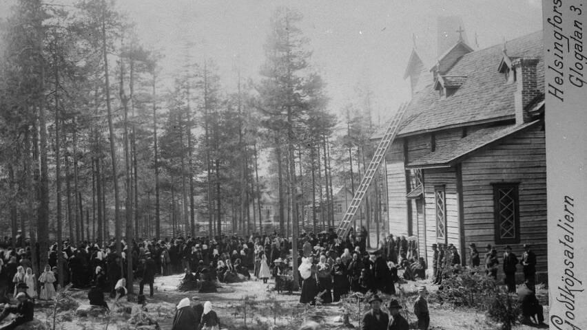 Mustavalkoinen kuva, jossa näkyy paljon väkeä ja vaalea kirkkorakennus, jonka katolle menee tikkaat.